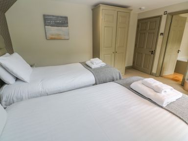 A bedroom with two single beds with white linens and folded towels next to a wardrobe and a door at Bodmin Country House in Lanivet