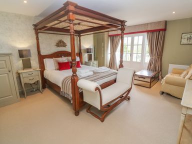 A bedroom with a four-poster bed a bench sofa nightstands and a window with curtains at Bodmin Country House in Lanivet