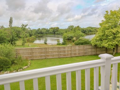A backyard with a wooden fence overlooking a pond and trees at Bodmin Country House in Lanivet