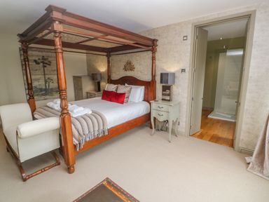 A bedroom with a wooden four poster bed a white armchair bedside tables with lamps and an open door to a bathroom at Bodmin Country House in Lanivet