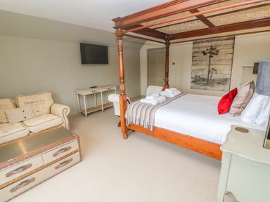 A bedroom with a four-poster bed, sofa, chest-style coffee table, wall-mounted TV and console table at Bodmin Country House Lanivet