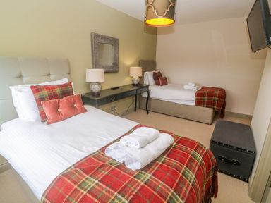 A bedroom with two single beds plaid blankets lamps on a black desk and a wall mounted television at Bodmin Country House Lanivet