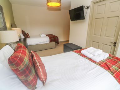 A bedroom with two beds a wall-mounted TV a door and bedside lamps at Bodmin Country House Lanivet
