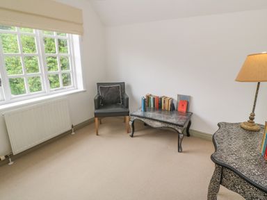 A room with a black armchair, two patterned tables with books and a lamp near a window at Bodmin Country House in Lanivet