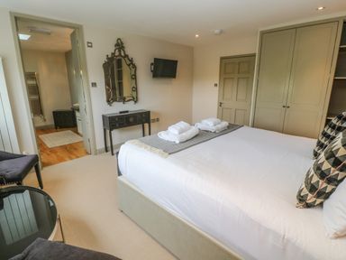 A bedroom with a large bed towels on the bed a black dresser mirror a wall mounted tv two chairs a small round table and an open door to a bathroom at Bodmin Country House Lanivet