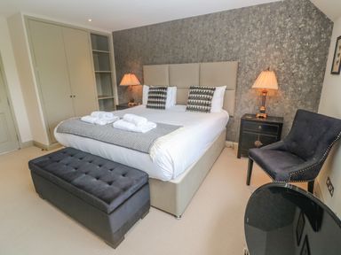 A bedroom with a bed folded towels on it a black bench a black chair a bedside table with a lamp and a wardrobe at Bodmin Country House Lanivet