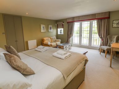 A bedroom with a bed with folded towels a sofa a table and large windows with curtains at Bodmin Country House Lanivet