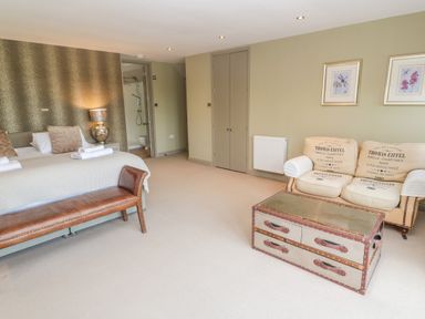 A bedroom with two beds a brown bench a sofa with printed cushions and a chest used as a table at Bodmin Country House in Lanivet