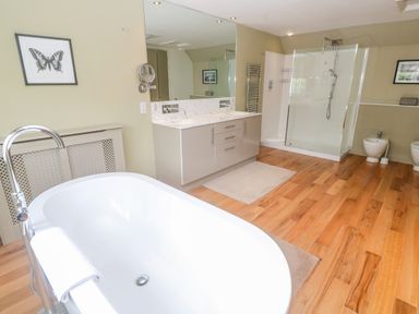 A bathroom with a bathtub, double sink vanity, glass shower, bidet, and wooden floor at Bodmin Country House in Lanivet