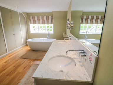 A bathroom with a freestanding bathtub under a window and a double sink vanity with a marble countertop at Bodmin Country House in Lanivet