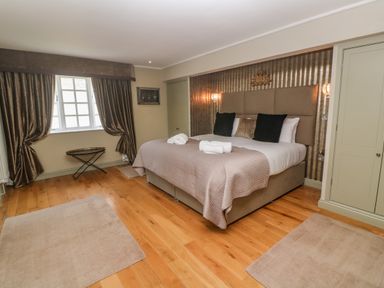 A bedroom with a bed with pillows towels on it two rugs on wooden floor curtains at the window and closets Bodmin Country House Lanivet