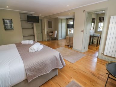A bedroom with a bed with towels on it a desk chair a floor lamp wooden floors and a bathroom at Bodmin Country House in Lanivet