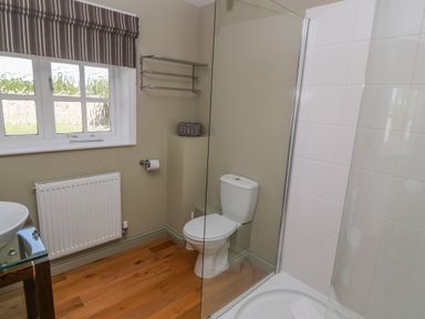 A bathroom with a toilet a shower a window with a striped blind a towel rack and wooden flooring at Bodmin Country House in Lanivet