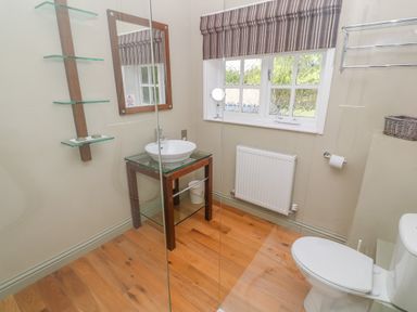 A bathroom with a wooden floor a toilet glass sink with a mirror and a window with striped blinds at Bodmin Country House in Lanivet