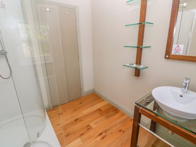 A bathroom with a glass shower, wooden floor, a sink with a wooden frame and glass shelves at Bodmin Country House Lanivet