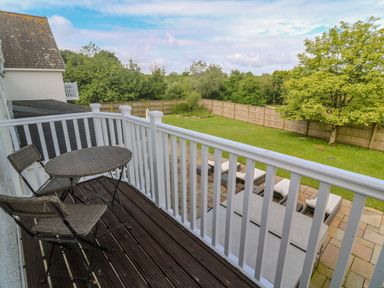 A small balcony with a round table and two chairs overlooking a garden with lawn chairs and trees at Bodmin Country House in Lanivet