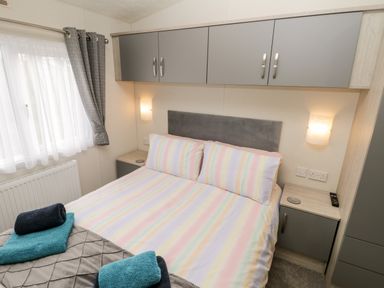 A bedroom with a double bed striped bedding bedside cabinets wall lamps and grey curtains at Lazy Daze in Carnaby near Bridlington