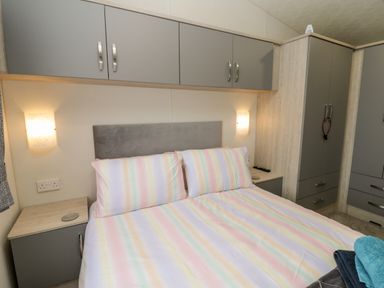 A bedroom with a double bed with pastel striped bedding and overhead cabinets at Lazy Daze Carnaby near Bridlington