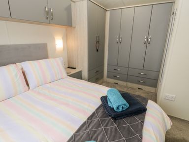 A bedroom with a bed with striped bedding and folded towels on top and gray wardrobes along the wall at Lazy Daze Carnaby near Bridlington