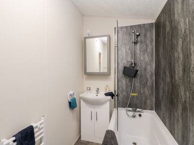 A bathroom with a bathtub shower combination a sink with storage a mirror cabinet and towels at Lazy Daze Carnaby near Bridlington
