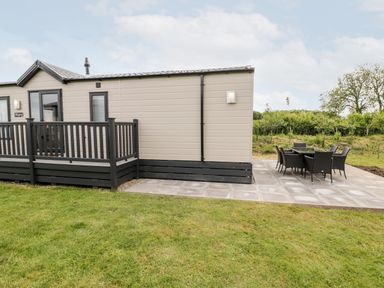 An outdoor patio area with a beige and black mobile home and a black dining table with six chairs on a stone tiled patio at Lazy Daze in Carnaby near Bridlington