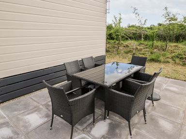 An outdoor patio area with a black wicker table and six matching chairs next to a beige building at Lazy Daze in Carnaby near Bridlington