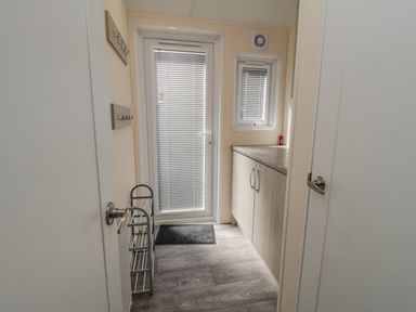 A small utility room with a door and window with blinds a cabinet countertop and door hooks in Brighter Daze Carnaby near Bridlington