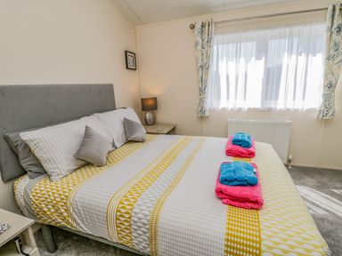 A bedroom with a bed with patterned bedding folded towels on it and a window with curtains at Brighter Daze Carnaby near Bridlington