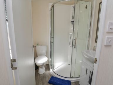 A bathroom with a toilet a curved glass shower enclosure a sink with cabinet and a blue bath mat at Brighter Daze Carnaby near Bridlington