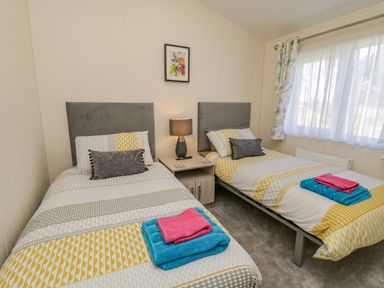 A bedroom with two single beds a nightstand and a window with curtains at Brighter Daze Carnaby near Bridlington