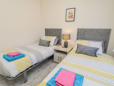 A bedroom with two single beds with patterned bedding and towels on them and a nightstand with a lamp between at Brighter Daze Carnaby near Bridlington