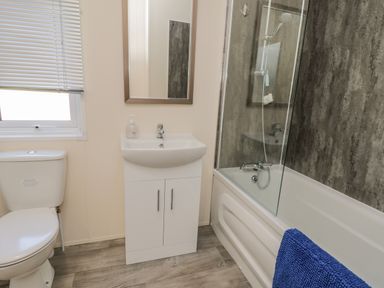 A bathroom with a toilet sink with cabinet mirror window and bathtub with shower and blue towel at Brighter Daze in Carnaby near Bridlington