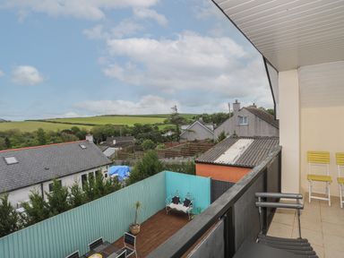 A balcony with chairs overlooking fenced backyards and houses with green fields in the background at The Old Coal Yard in Cemaes Bay
