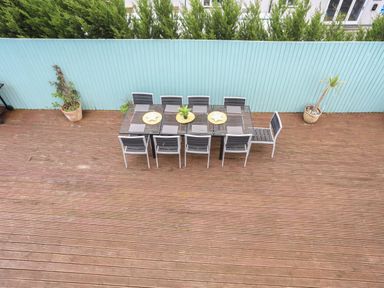 An outdoor wooden deck with a dining table and eight chairs two potted plants and a blue fence at The Old Coal Yard in Cemaes Bay