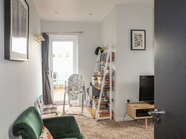A living room with a green armchair bookshelf and television at The Old Coal Yard in Cemaes Bay