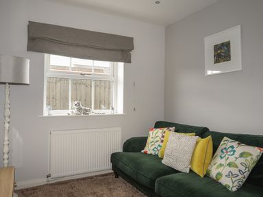 A living room with a green sofa and colorful cushions near a window with a white tiger figurine at The Old Coal Yard in Cemaes Bay