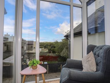 A room with a large window a grey armchair a pink table and a small plant at The Old Coal Yard in Cemaes Bay