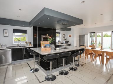 A kitchen with black island and stools next to a wooden dining table with chairs at The Old Coal Yard in Cemaes Bay