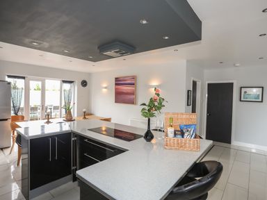 A kitchen with a countertop island with snacks and drinks a dining table by glass doors and black and white decor at The Old Coal Yard in Cemaes Bay