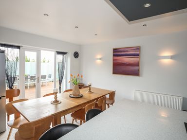 A dining area with a wooden table and chairs a vase with flowers a wall clock and an outdoor patio visible through glass doors at The Old Coal Yard in Cemaes Bay