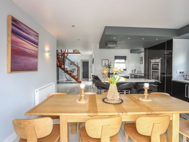 A dining table with wooden chairs and a flower vase in an open kitchen area with black cabinets and stairs at The Old Coal Yard in Cemaes Bay