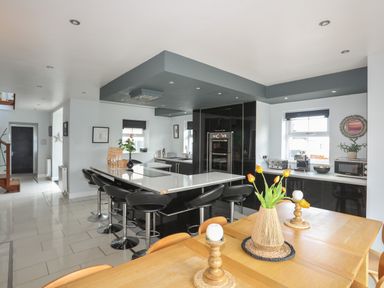 A kitchen and dining area with a black island and bar stools and a wooden dining table with flowers at The Old Coal Yard in Cemaes Bay