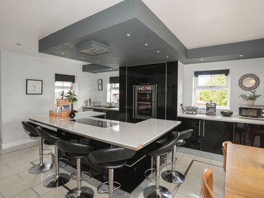 A kitchen with black cabinets and bar stools around a white island at The Old Coal Yard in Cemaes Bay