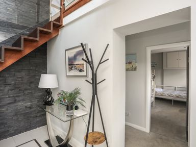 An entryway with a glass table lamp plant and coat rack near wooden stairs and a bedroom entrance at The Old Coal Yard in Cemaes Bay