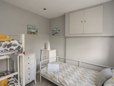 A small bedroom with bunk beds a single bed two white dressers and paintings on the wall at The Old Coal Yard in Cemaes Bay