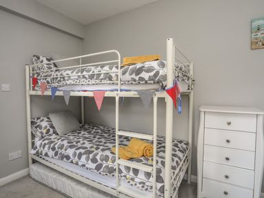 A bunk bed with leaf patterned bedding and yellow towels next to a white chest of drawers at The Old Coal Yard in Cemaes Bay