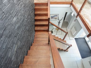 A staircase with wooden steps and a black textured wall leading to a lower floor with white tiles and a black mat at The Old Coal Yard in Cemaes Bay
