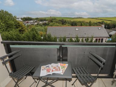 A balcony with two chairs and a table with magazines overlooking houses and green hills at The Old Coal Yard in Cemaes Bay