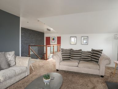 A living room with two sofas and a coffee table near a staircase with a glass railing at The Old Coal Yard in Cemaes Bay