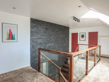 A stairway landing with glass and wood railing two red doors and framed artwork on walls at The Old Coal Yard in Cemaes Bay